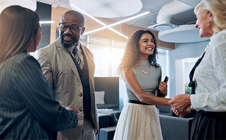 Four people in a modern office shaking hands and smiling.