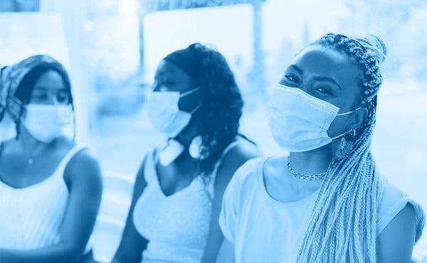 Three young Black women socializing while wearing paper face masks