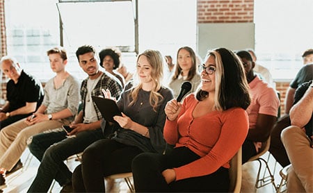 An audience, with a person in the foreground holding a microphone and smiling.