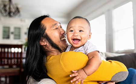 A happy baby being held, looking over his father's shoulder