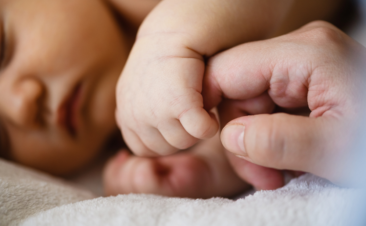 A baby's hand gently touches an adult's hand, symbolizing connection and tenderness.