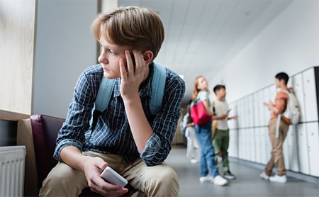 A boy sits alone in a school hallway, looking sadly out the window