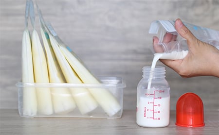 A bag of breast milk is emptied into a bottle, 5 extra bags in the background