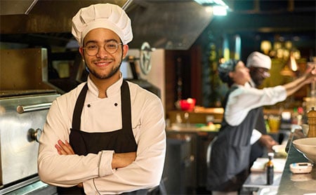 Chef facing the camera standing smiling with arms crossed in a restaurant kitchen
