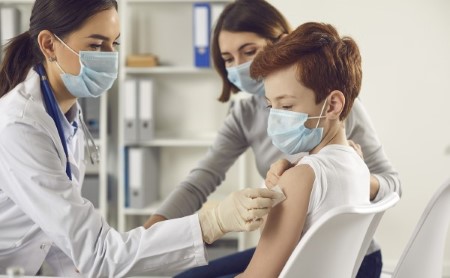 Doctor in medical face mask giving vaccine injection to young child