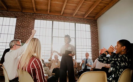 Group of people sitting in a circle of chairs with a trainer standing in the middle.