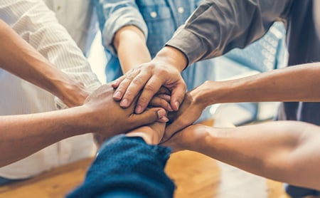 Diverse coworkers put their hands in the center of a circle to symbolize successful teambuilding