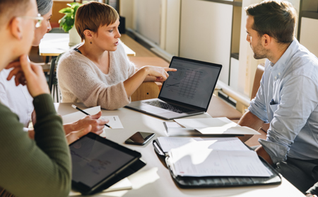 Coworkers sit around a conference table examining data on a laptop