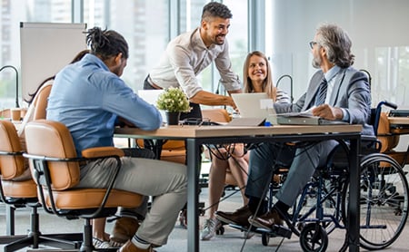 A diverse group of coworkers, including a man in a wheelchair, work collaboratively at the office