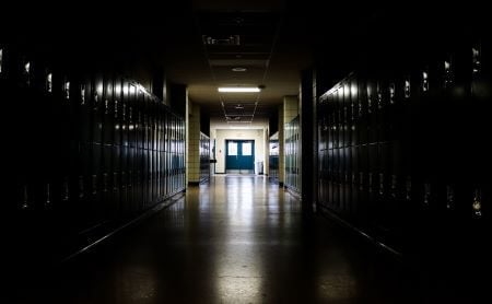 Darkly lit hallway with bright light at the end, school lockers along the side walls