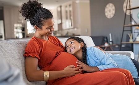 Adolescent daughter leaning on mother with pregnant belly