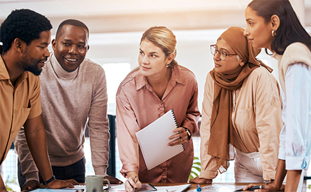 A diverse group of cowkers stand over a conference table planning out a project