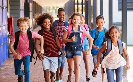 A diverse group of happy children run down on outdoor school hallway