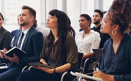A diverse group of young professionals sit in a seminar audience