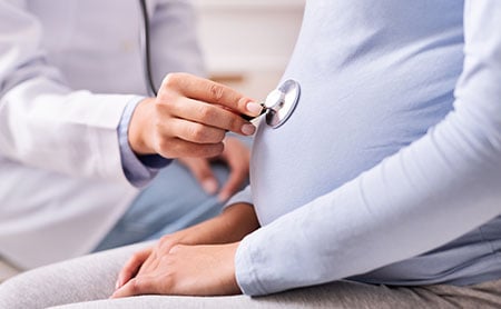 Doctor placing stethoscope on pregnant belly