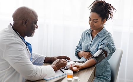 Doctor checking a woman's blood pressure over a desk