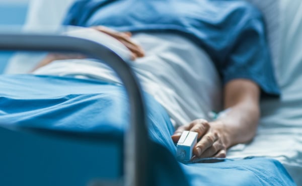 Midsection of elderly person laying in a hospital bed with oximeter on their finger