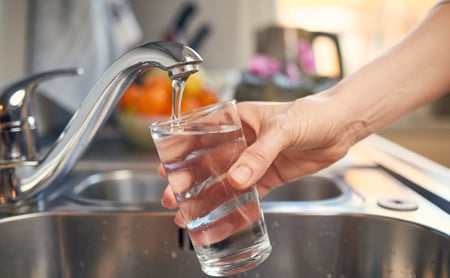 Hand holding a glass of water while it is being filled at a kitchen sink