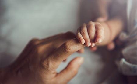 A baby's hand holding one of its mother's fingers