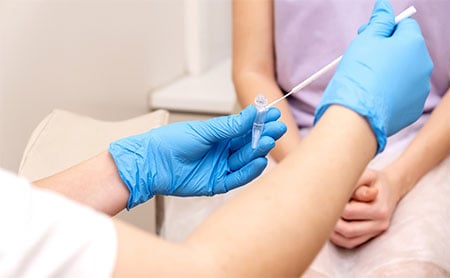 Healthcare professional with blue gloves holding a cotton swab and vial near a patient's arm.