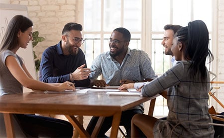 Group of young, diverse colleagues sitting around a wooden table having a discussion