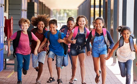 A group of happy, young students runs down a school portico