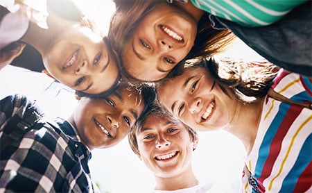 A group of five kids smiling down at the camera against a clear sky.