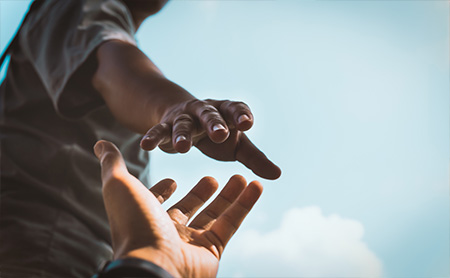 Two outstretched hands, one reaching to help the other up