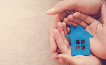 Child hands holding a paper house while nested in an adult hand