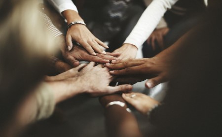 Image of adult officemates putting their hands in the middle of a team huddle, team-building cheer