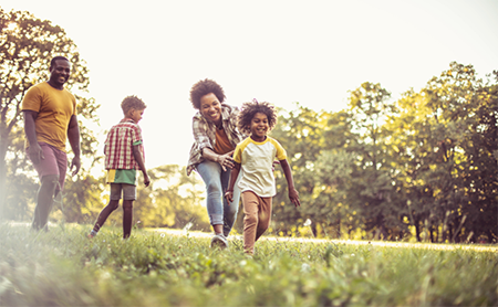 A happy Black family of four plays outside in a park in the summer