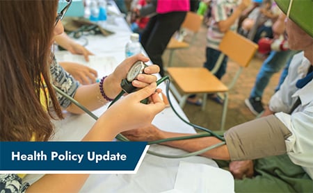 A community health worker takes someone's blood pressure at a clinic. ASTHO Health Policy Update banner in lower left