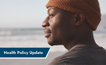 Man in a beanie stands on the beach looking at the ocean. ASTHO HPU banner in the lower left