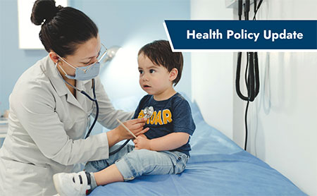 Masked female pediatrician placing stethoscope on a little boy's chest in a doctors office