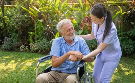 Smiling healthcare worker outside with her patient in a wheelchair