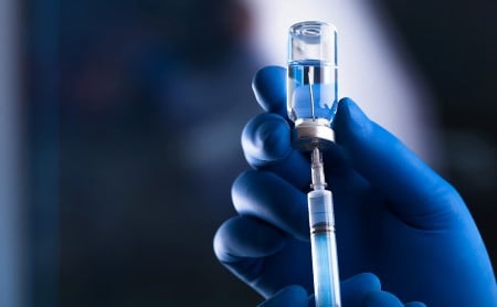 Gloved hand of healthcare professional using syringe to remove medicine from ampoule