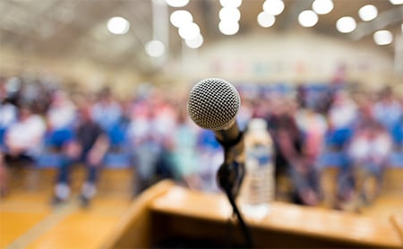 Focused shot of a microphone on a speaker's podium at a large public meeting