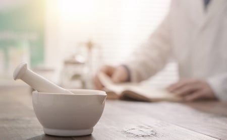 Mortar and pestle in the foreground, out-of-focus pharmacist visible in the background