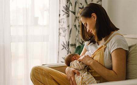 A mother breastfeeds her baby at home on the couch