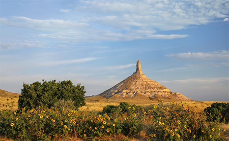Chimney Rock in Nebraska with sunflowers and a blue sky.