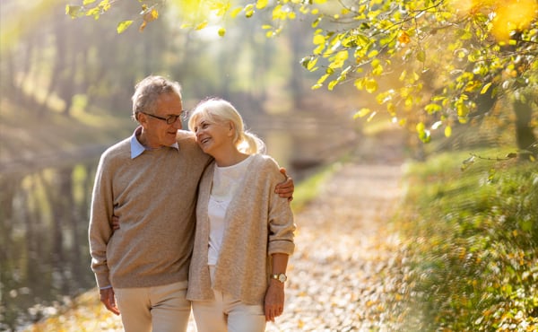 An older couple walks along a stream in the fall