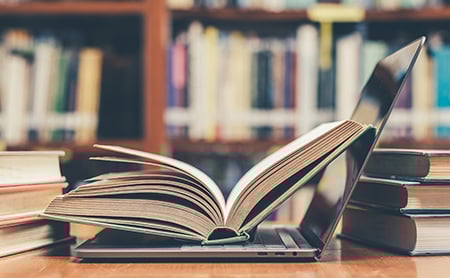 Open book laying on top of an open laptop