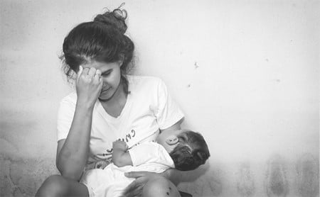 Black and white image of an overwhelmed young mother holding baby to her chest