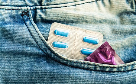 Blister package of pills and a condom visible at the top of someone's pocket