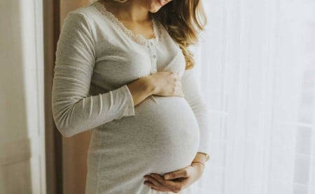 Midsection shot of a pregnant woman cradling her belly, smiling