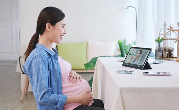 A smiling expectant mother has a telehealth appointment at her kitchen table