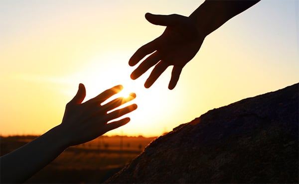 Silhouette of two hands reaching toward one another at sunset