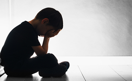 A small boy seated on the floor with his head in his hands