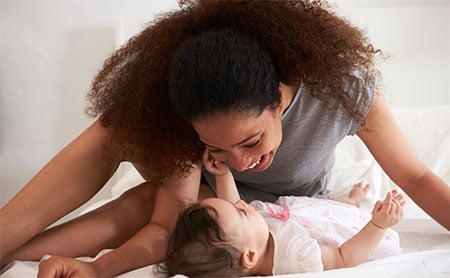 Smiling mom leaning over baby in a pink dress laying on a table.