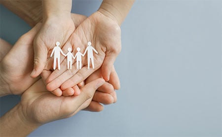 Child's hands holding paper dolls resting inside an adults hands, palms face up